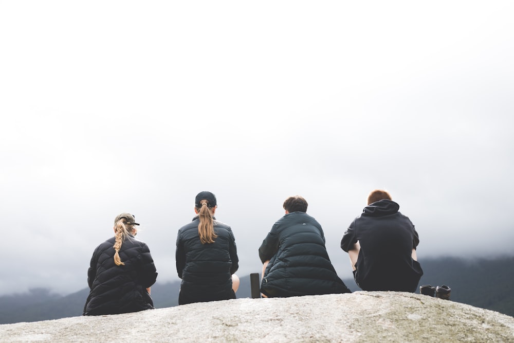 four persons sitting on gray rock