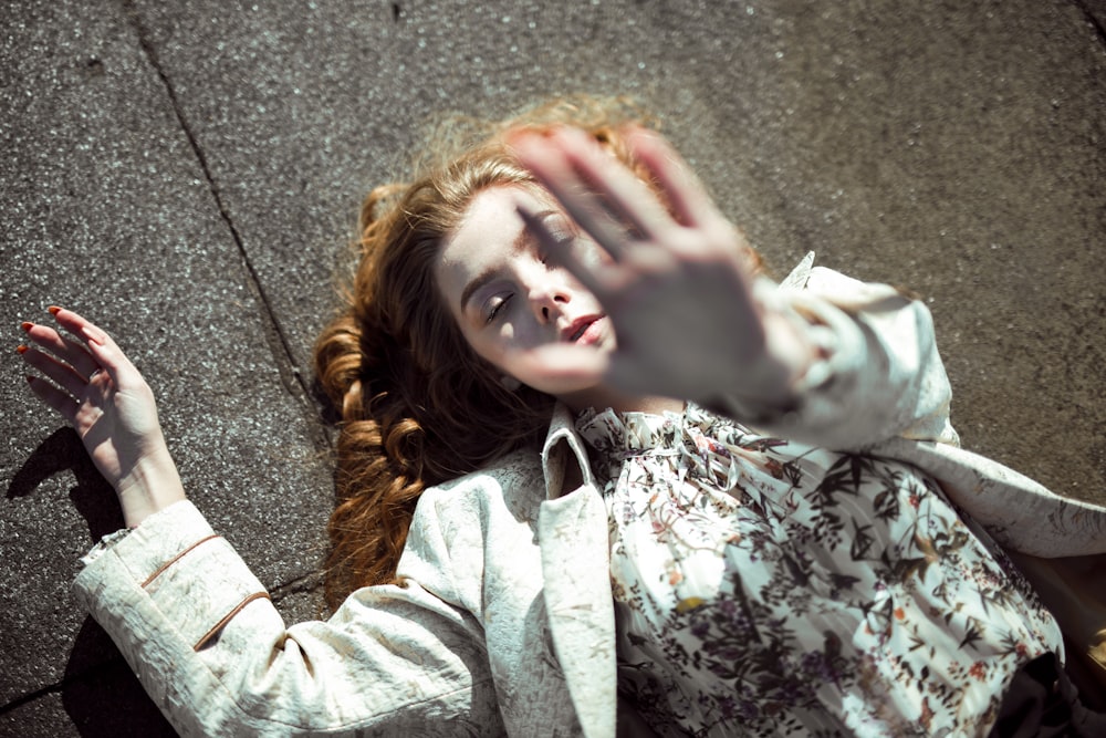 woman lying on concrete pavement and raising her left hand