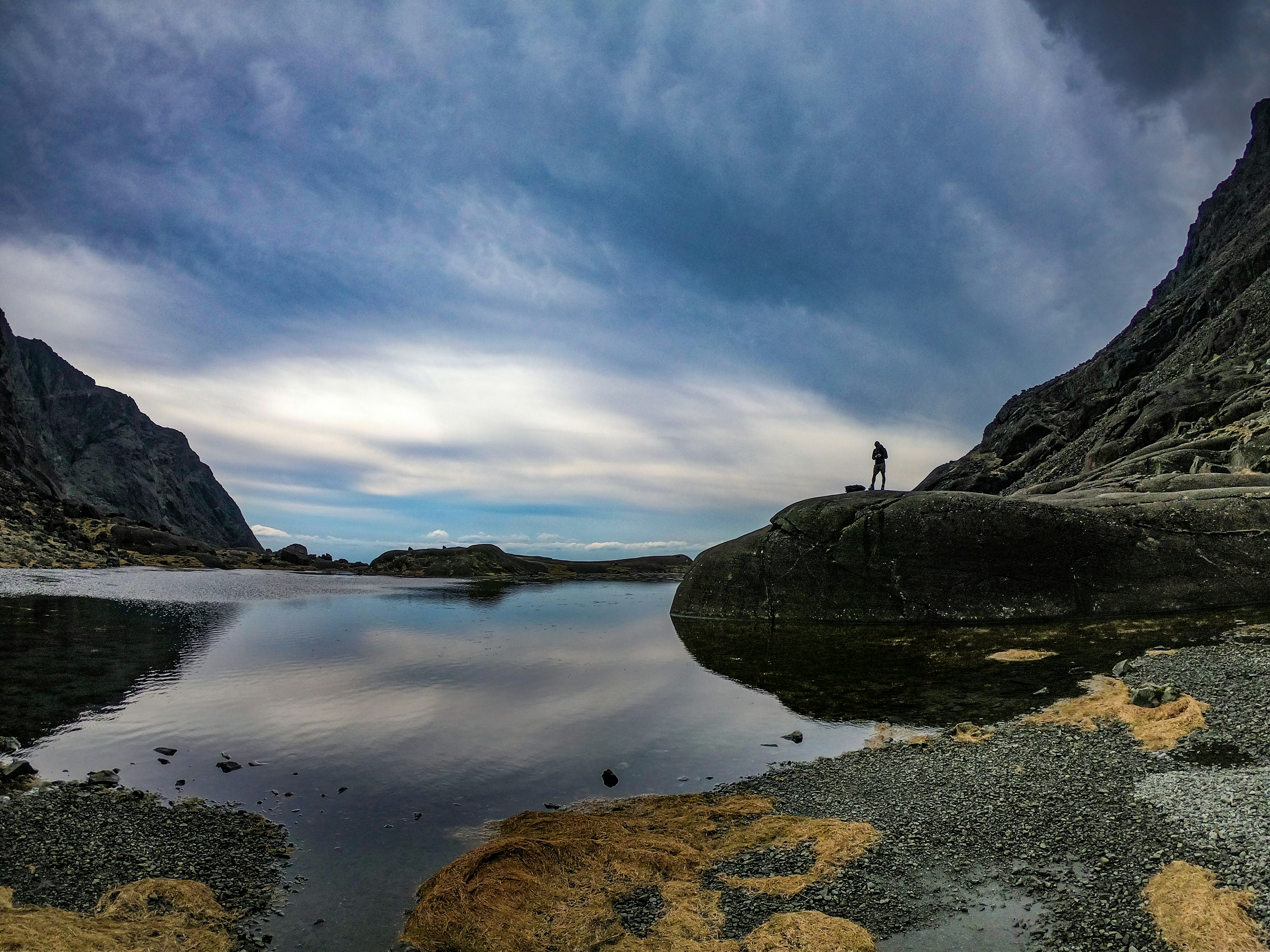 Solo hiker standing at edge of cliff overlooking Patagonian lake system under dramatic storm clouds