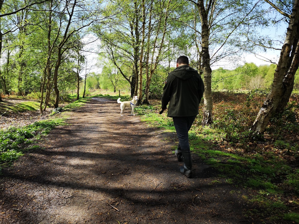 man walking on dirty road and white dog in front during daytime