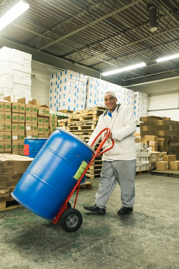 Warehouse worker moving a labeled chemical drum past stacked inventory