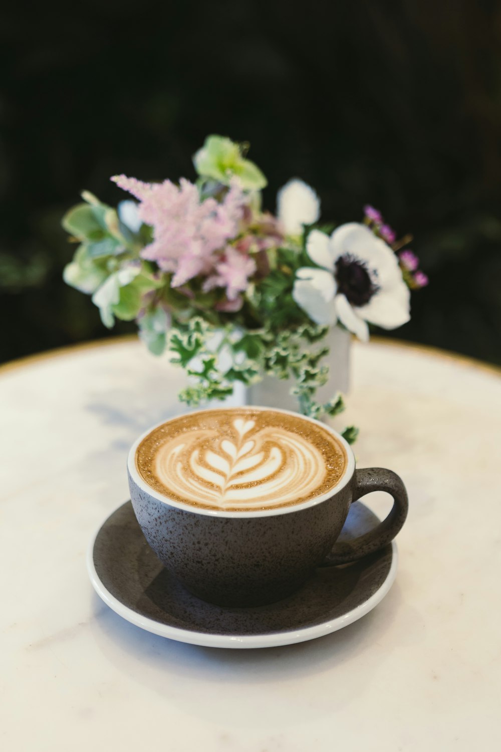 Tasse Cappuccino auf Untertasse neben Blumenaufsatz