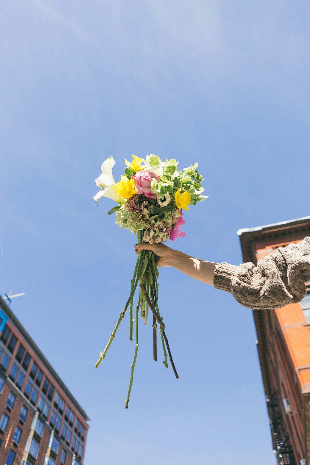 person in grey knit sweater holding bouquet of flowers