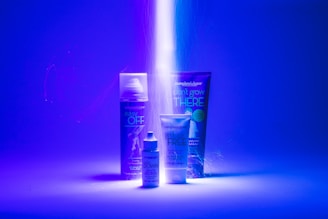 A striking visual setup featuring three personal care products with bright, neon lighting. The background is predominantly blue, and a beam of light illuminates the products, enhancing their labels. Each item is distinctly visible with a modern and sleek design.