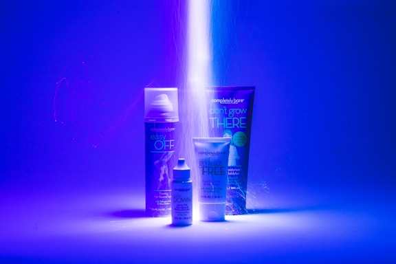 A striking visual setup featuring three personal care products with bright, neon lighting. The background is predominantly blue, and a beam of light illuminates the products, enhancing their labels. Each item is distinctly visible with a modern and sleek design.