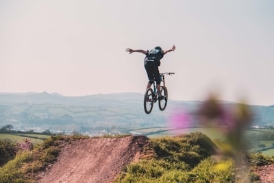 An action shot of a rider catching air off a dirt ramp, with rugged terrain stretching behind.