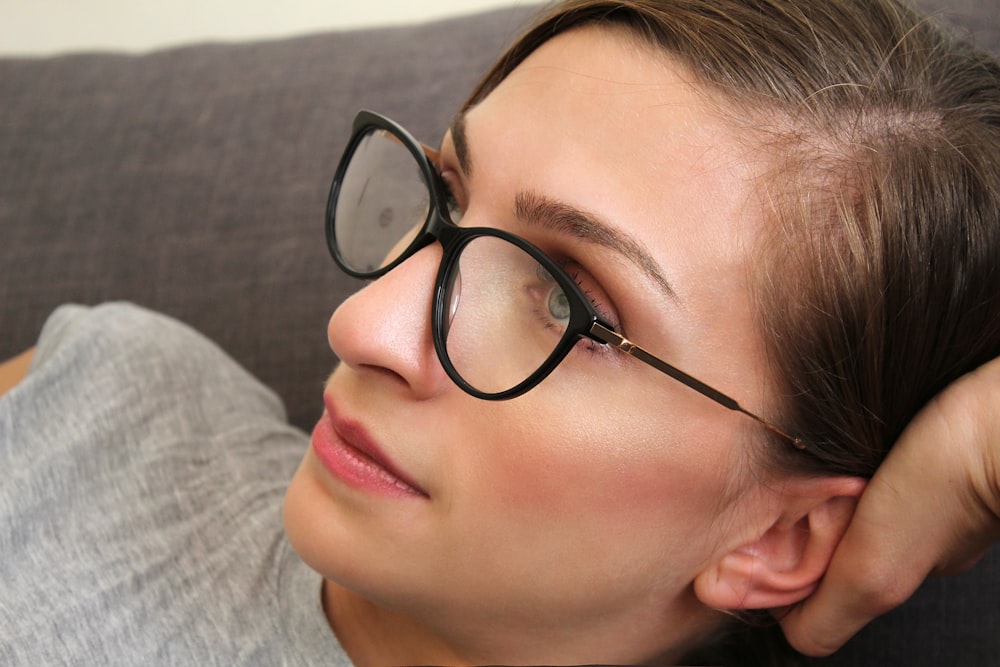 woman wearing black framed eyeglasses and grey shirt lying on bed
