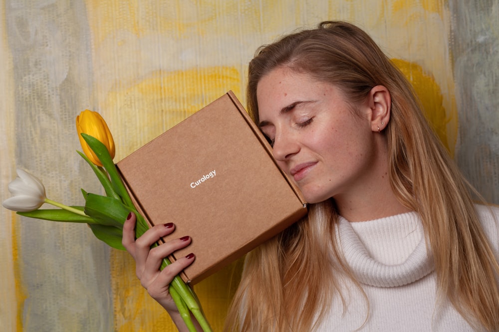 Femme en pull blanc tenant une boîte marron et des fleurs de tulipe