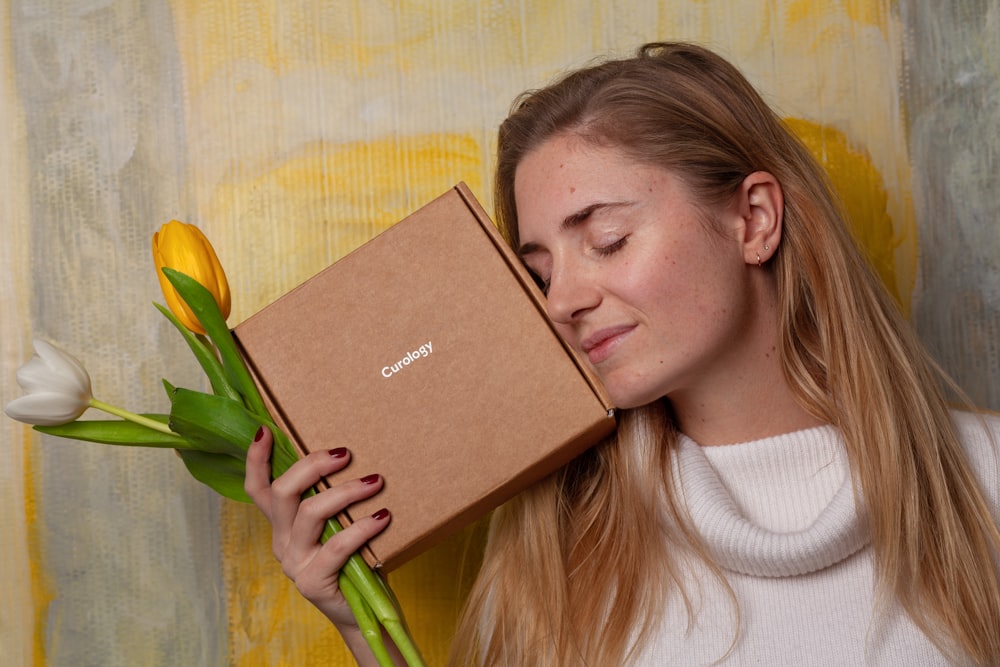 woman in white sweater holding brown box and tulip flowers