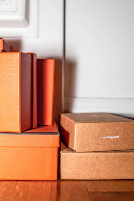 A stack of vivatela tissue boxes with unique patterns displayed on a wooden shelf in a bright room.