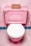 A pink toilet with a white seat is set against pink tiled walls and floor. On top of the toilet tank, there is a small, brown cardboard box.