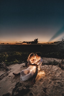 photography poses for couples,how to photograph man and woman looking each other sitting on white sand during sunset