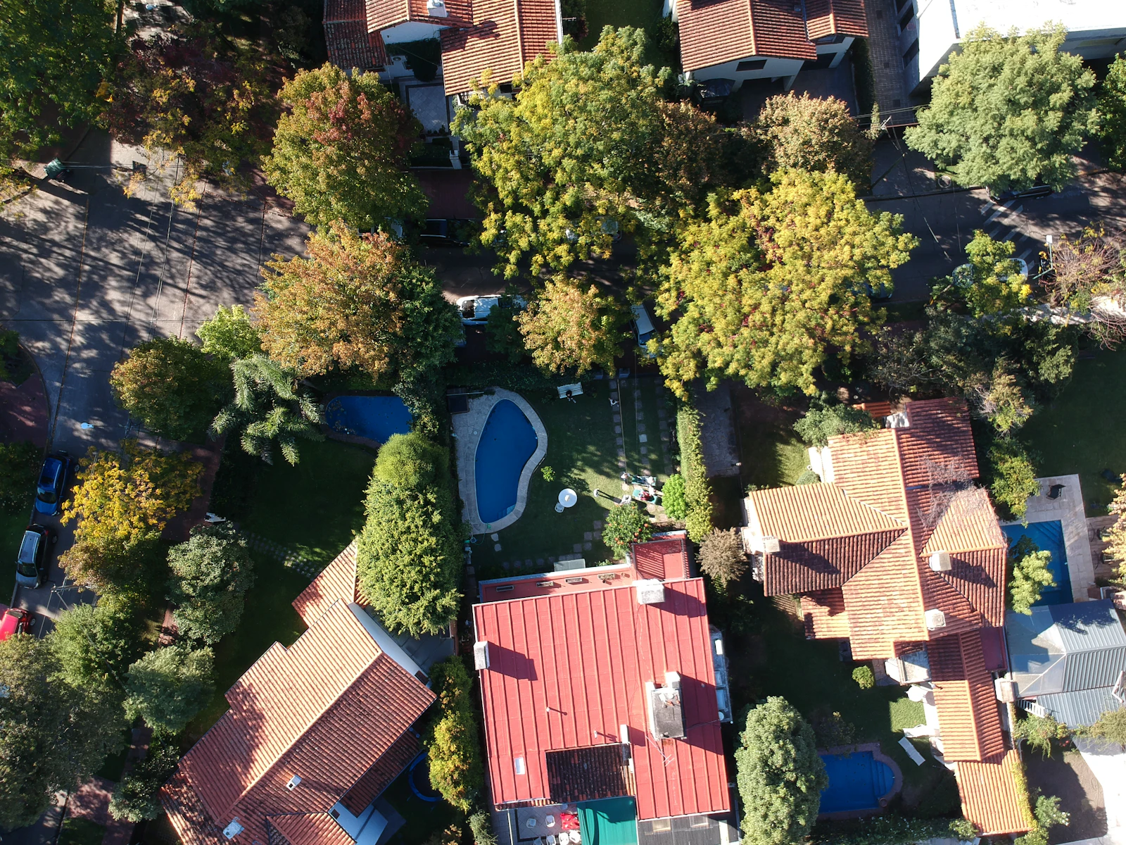 Vista aérea de bairro residencial: casas com telhado de telha, quintais com piscina e ruas arborizadas.