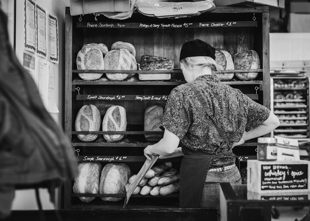 fotografia in scala di grigi di donna in piedi sullo scaffale del pane