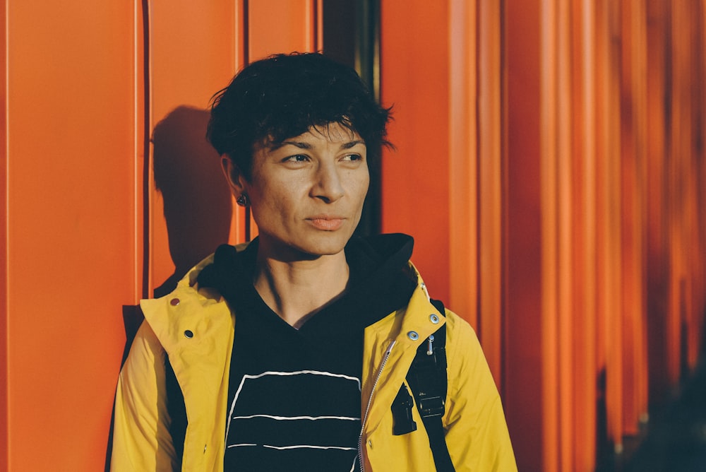 woman in yellow jacket leaning on orange wall