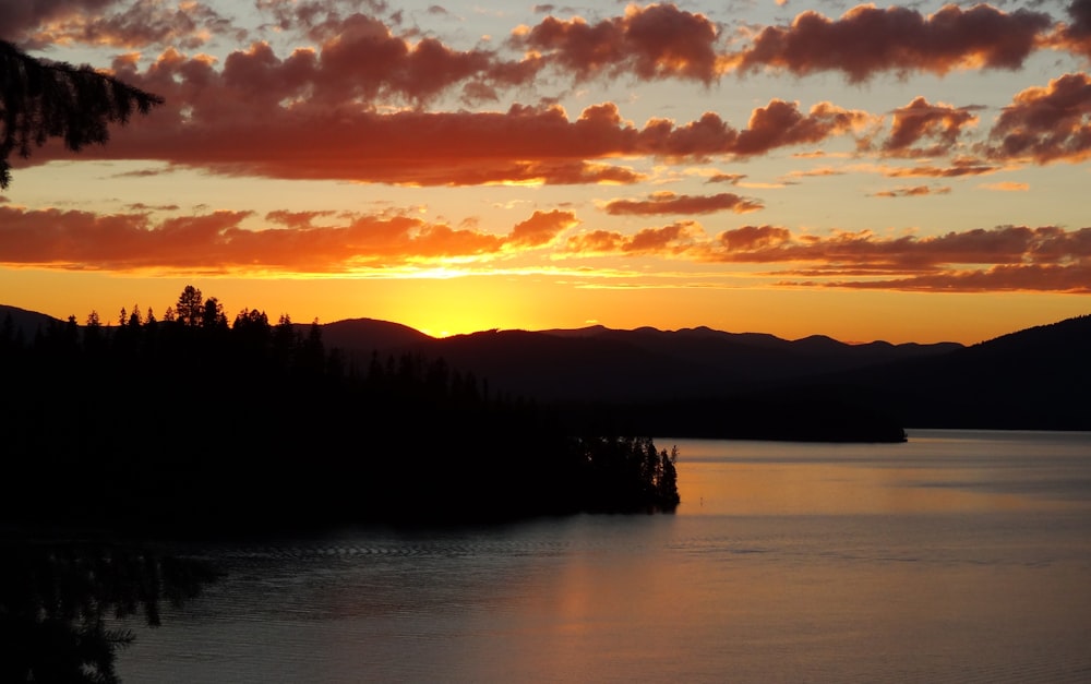 the sun is setting over a lake with mountains in the background