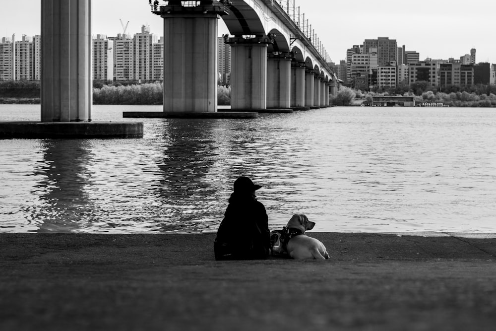 person sitting beside dog near body of water