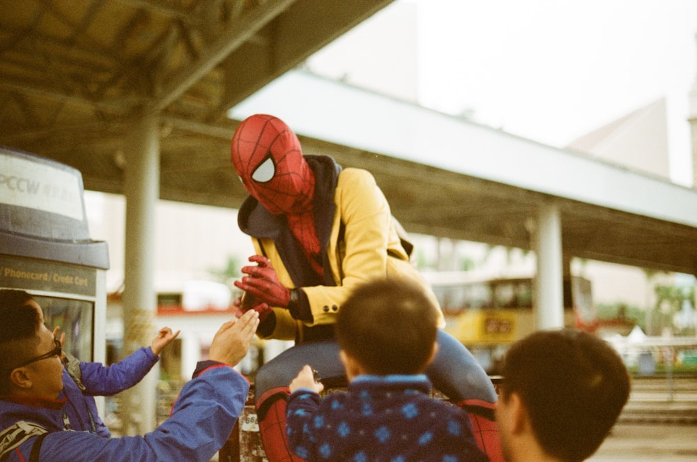 Un hombre disfrazado de Spider Man le está entregando algo a un niño