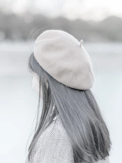 A model wearing a soft beige beret, smiling against a city street backdrop.
