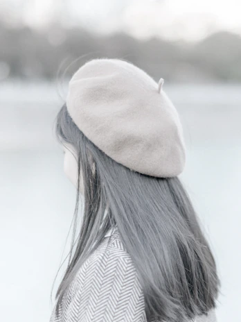 A model wearing a soft beige beret, smiling against a city street backdrop.