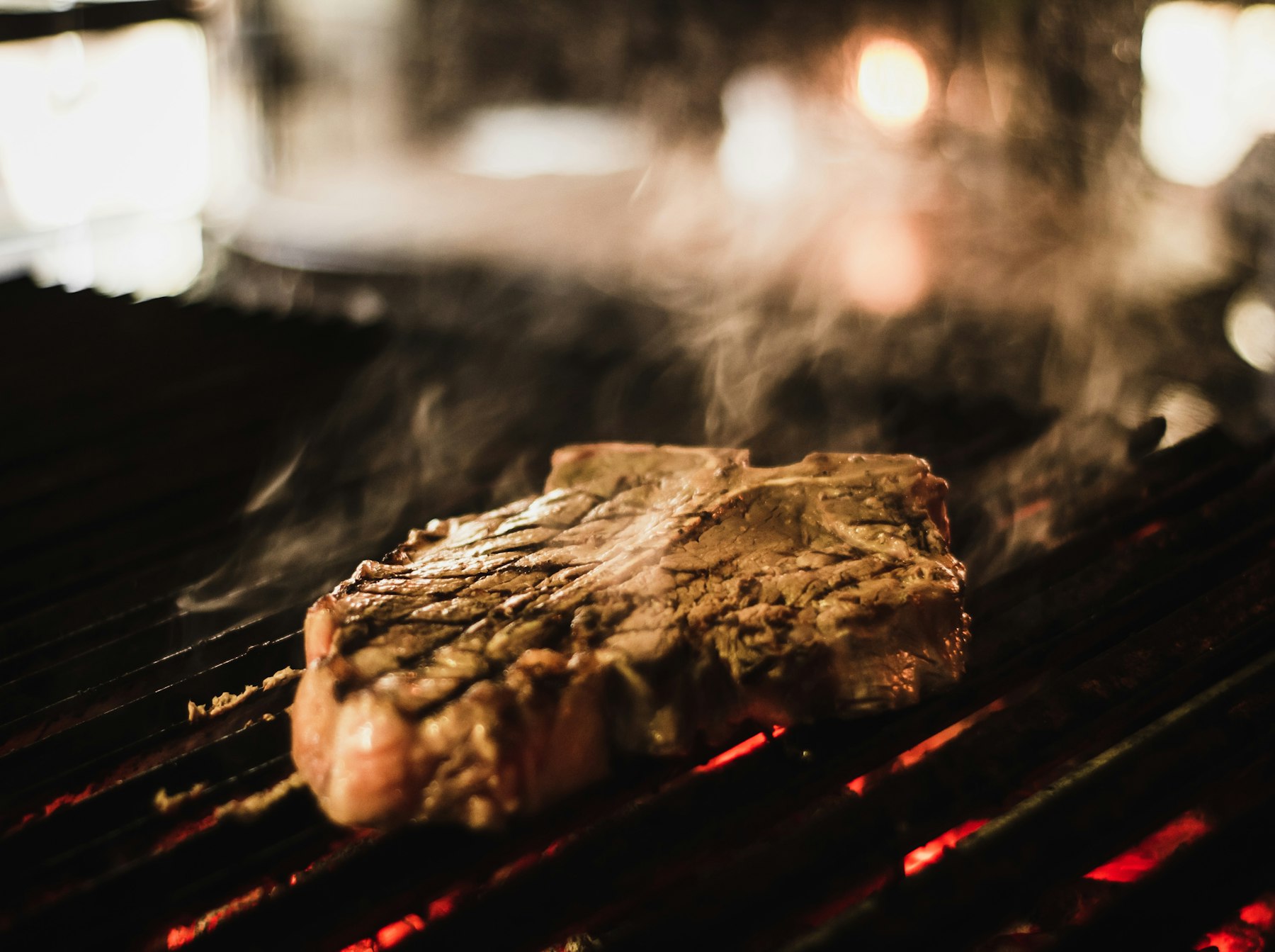 Dry-aged chop searing over open coals, steam rising - Ember & Salt, Charleston SC