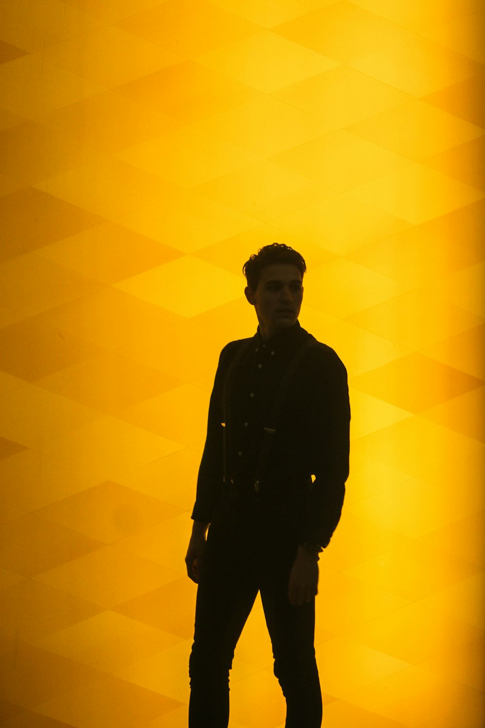 man wearing black dress shirt standing near yellow background