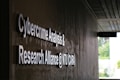 Signage on a wall reads 'Cybercrime Analysis & Research Alliance @ NTU (CARA)' in bold, white letters against a dark, textured surface. A corridor with partial ceiling panels is visible, and there's some greenery in the background.
