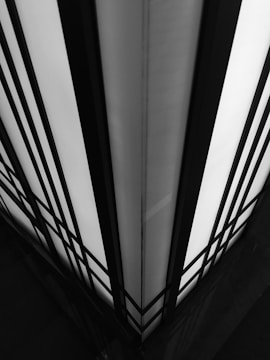 A symmetrical, high-contrast black and white image featuring geometric patterns with vertical and horizontal lines converging at an angle. The lines create a sense of depth and architectural design.