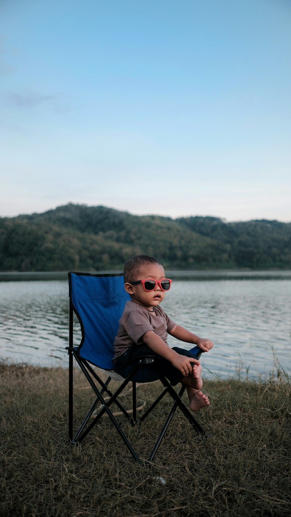 Chico con camisa gris sentado en una silla de camping azul cerca del cuerpo de agua