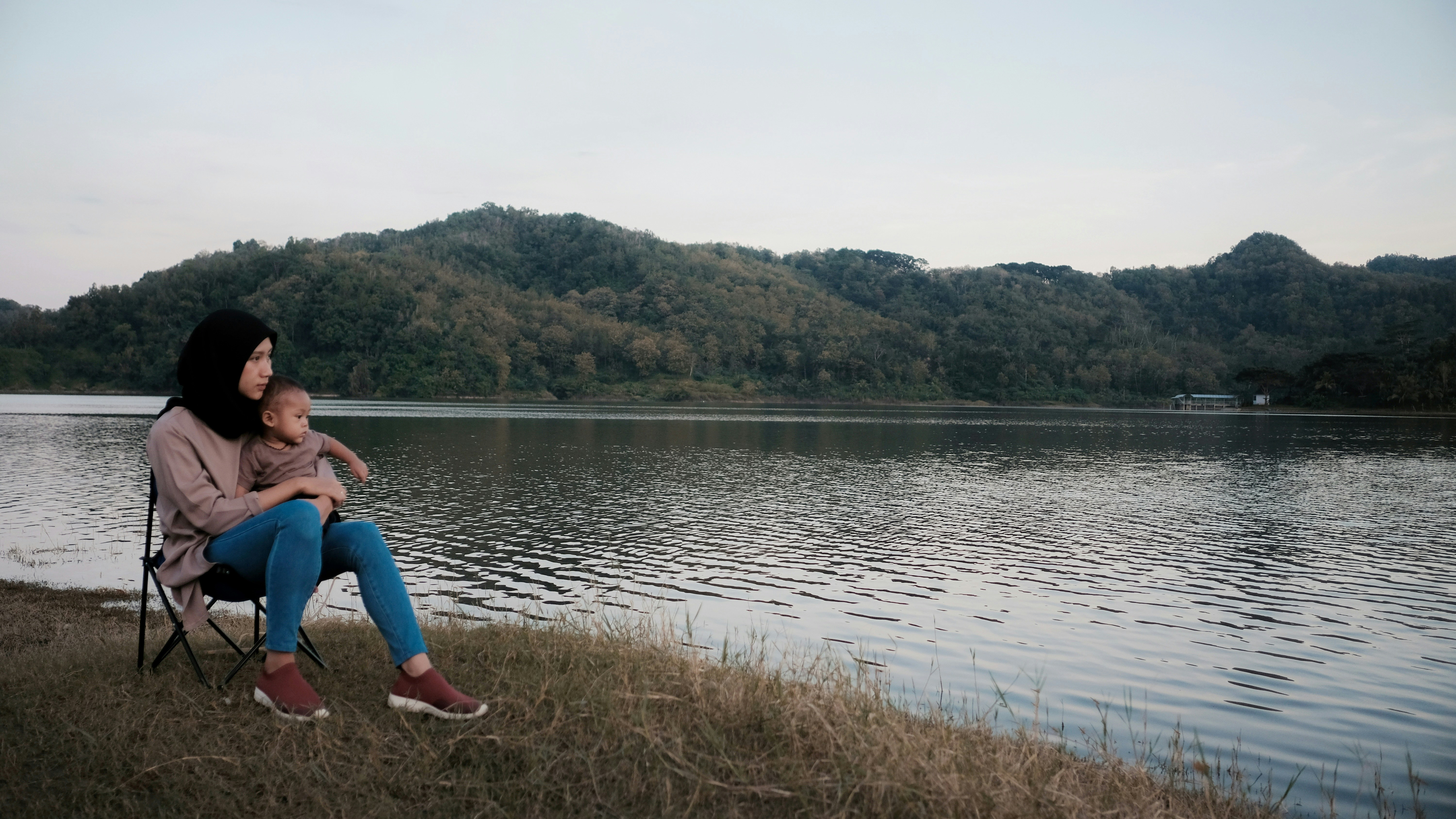 woman carrying baby near body of water during daytime