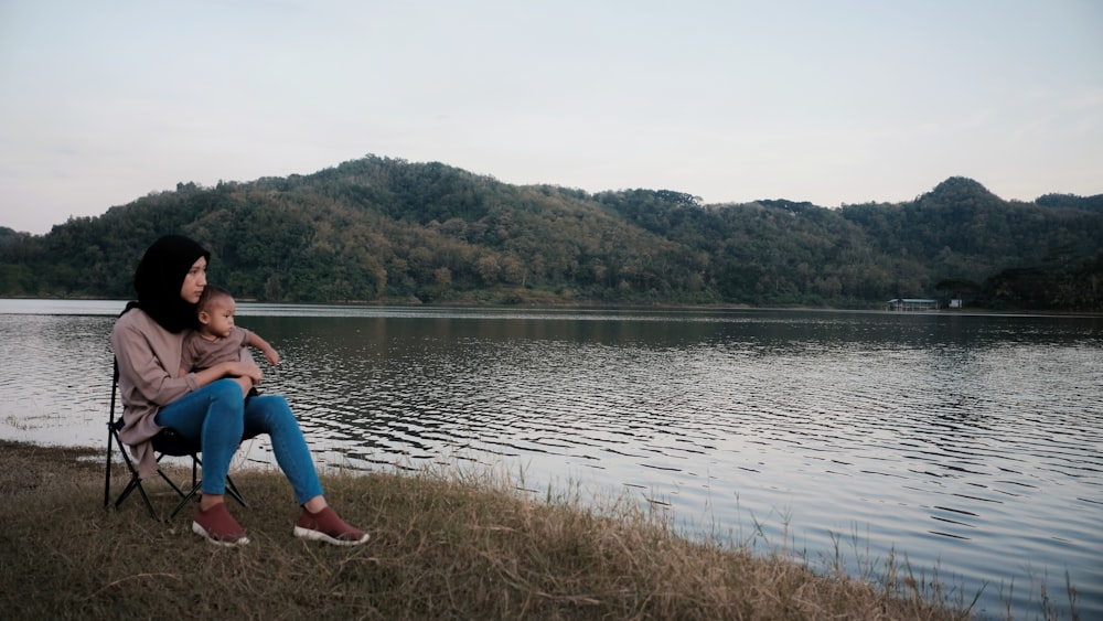 woman carrying baby near body of water during daytime