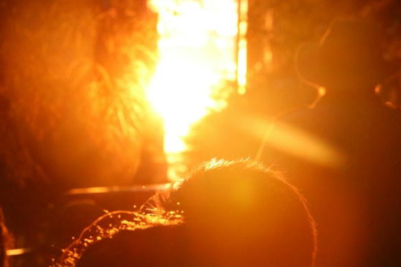 The image captures a bright, glowing sunlight that creates a silhouette effect on the person in the foreground. The intense golden light fills the scene, casting warm shades and producing lens flares.