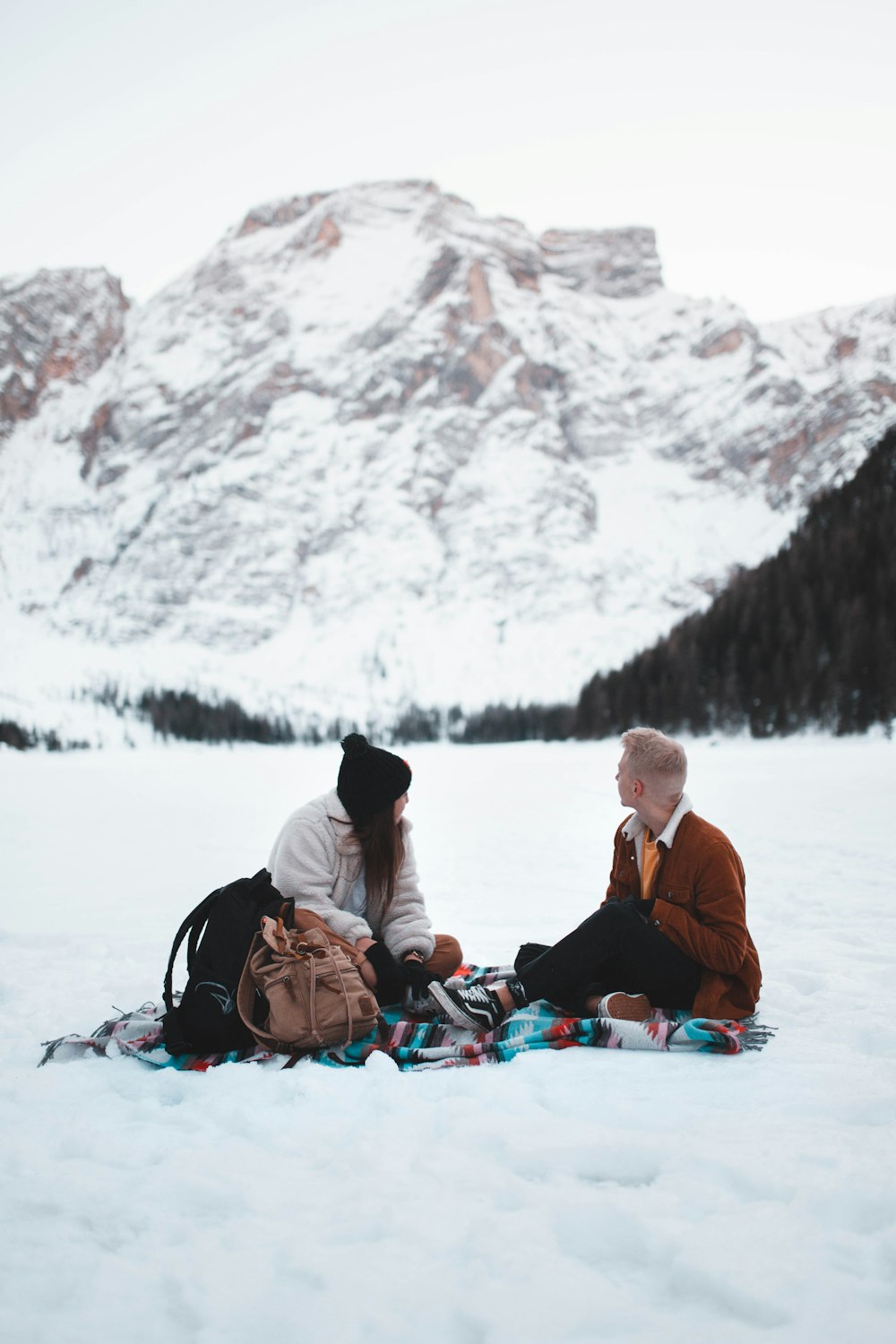 man and woman sitting in middle of snow field during daytime