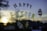 Colorful letters spell out 'Happy Easter' against a window with a view of a sunset or sunrise in the background. Decorative Easter eggs surround the text, and there is a blurred silhouette of trees and buildings.