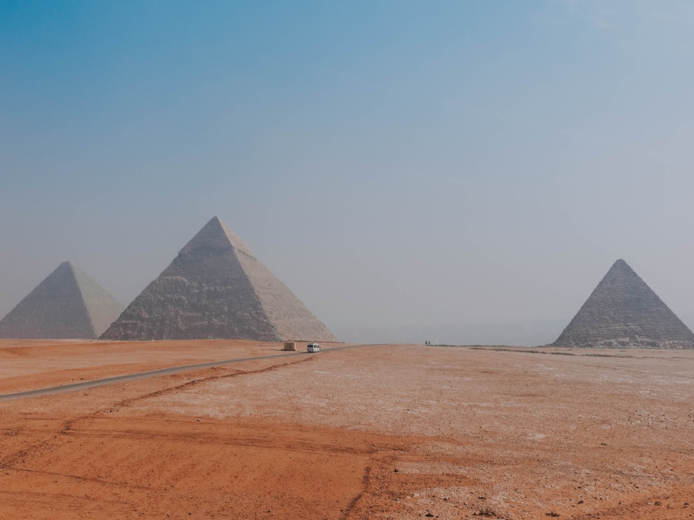 two vehicle on desert overlooking three pyramid at daytime