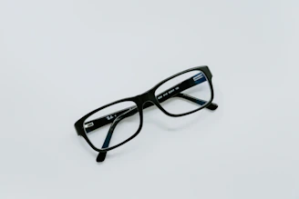 Close-up of sleek black optical frames resting on a white surface with subtle deep blue accents.