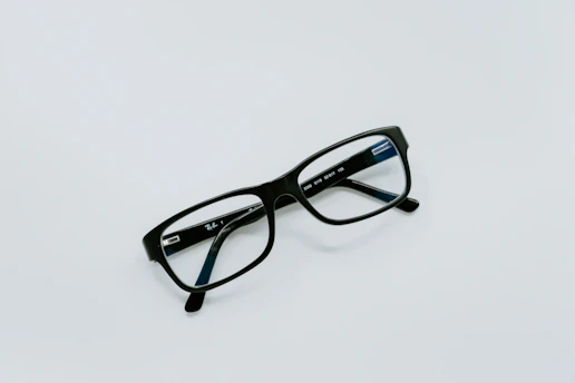 Close-up of sleek black optical frames resting on a white surface with subtle deep blue accents.