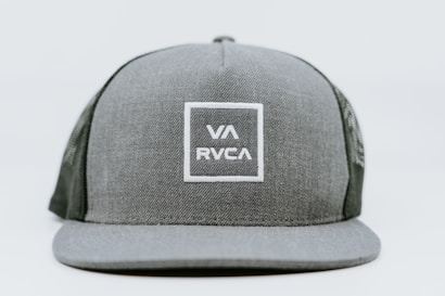 A gray baseball cap featuring a structured front panel with a mesh back. The front is adorned with a square logo containing the letters VA and RVCA in white stitching.