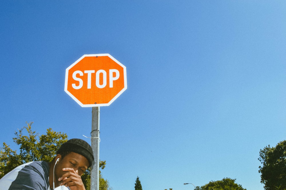 man in grey and white shirt stands under red and whtie stop road sign