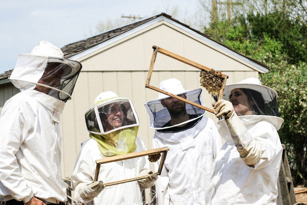four people in anti-bee bite suit holding honeycomb during daylight