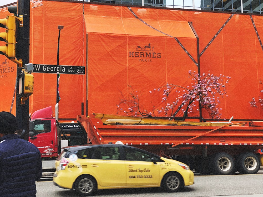 yellow hatchback passing by orange freight truck