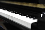 A close-up view of a piano keyboard, with both black and white keys clearly visible. The image captures the sheen on the keys, suggesting a well-maintained or new instrument.