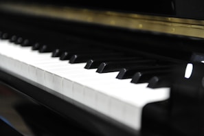 A close-up view of a piano keyboard, with both black and white keys clearly visible. The image captures the sheen on the keys, suggesting a well-maintained or new instrument.