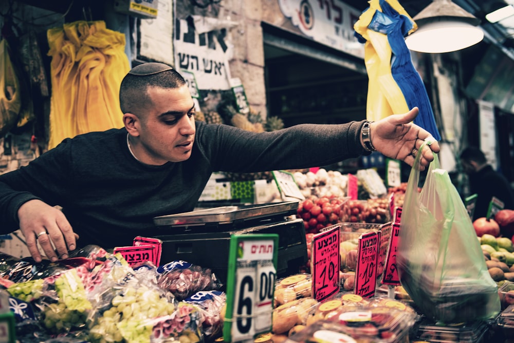 man reaching out with green plastic bag on hand over assorted fruits display