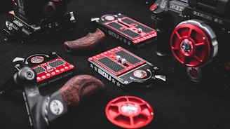 Various components and gears, featuring a range of intricate designs, are arranged on a dark surface. These items include detailed metal pieces with red and black color schemes, some with engraved patterns, suggesting they are parts of high-end equipment.