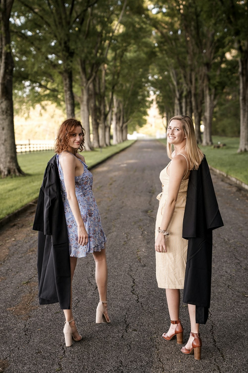 two women walking on road near trees