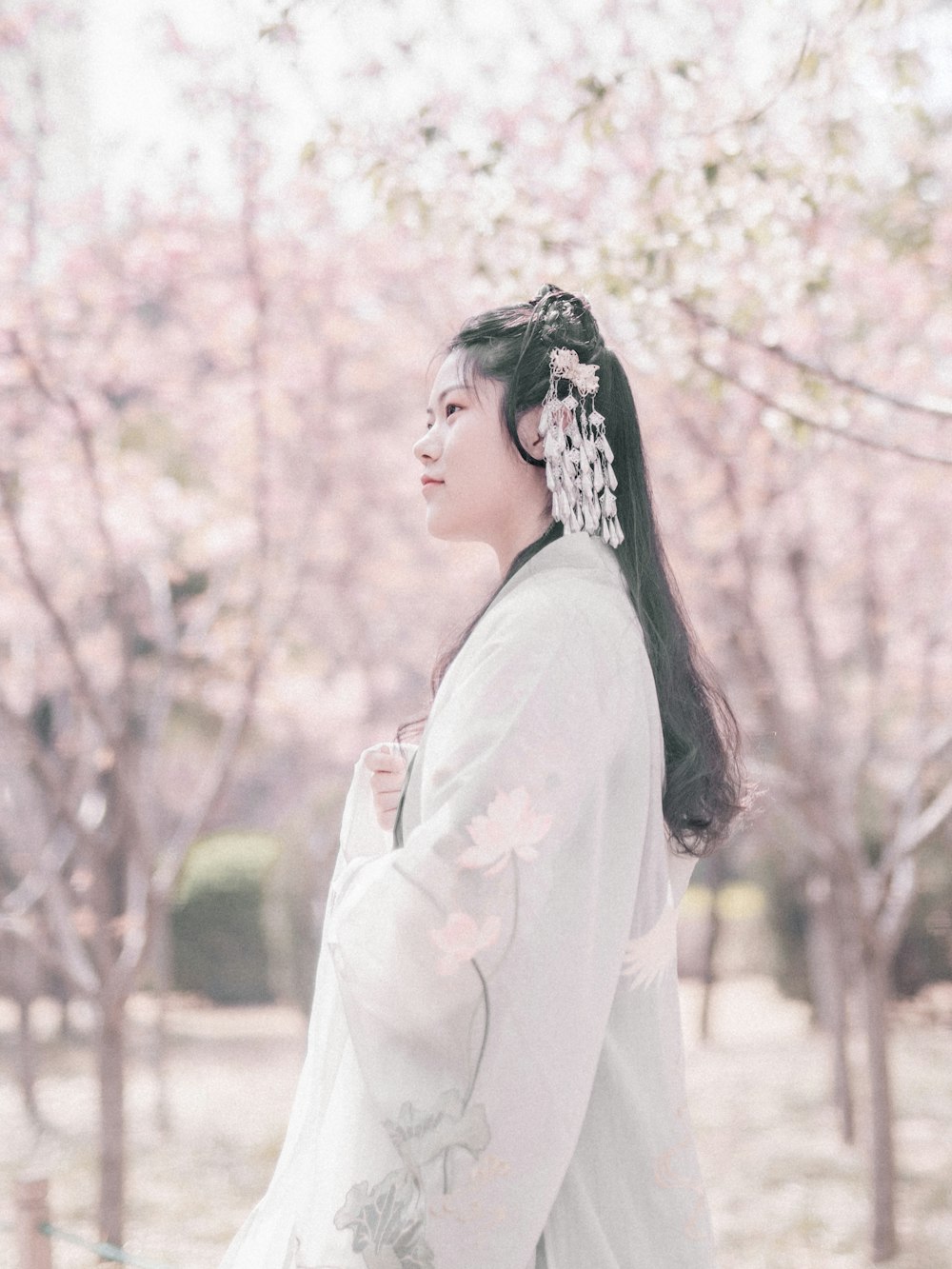 woman in white dress stands under blooming pink cherry blossom trees