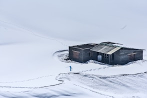 grey wooden cottage in middle of white snow covered field