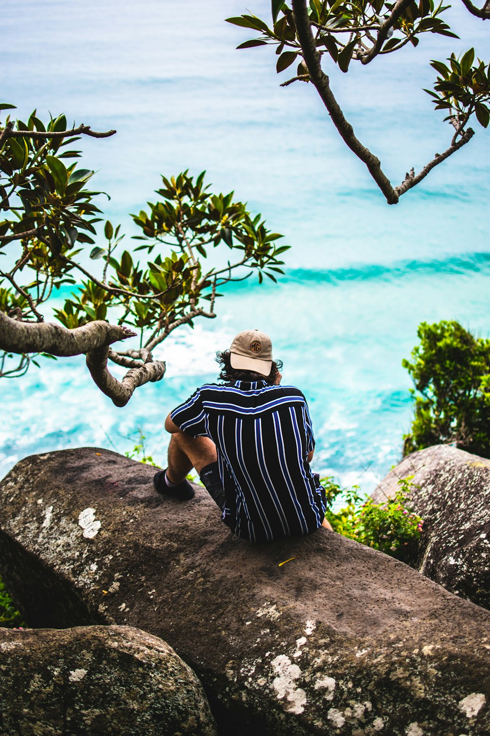 man sitting on rock above body of water