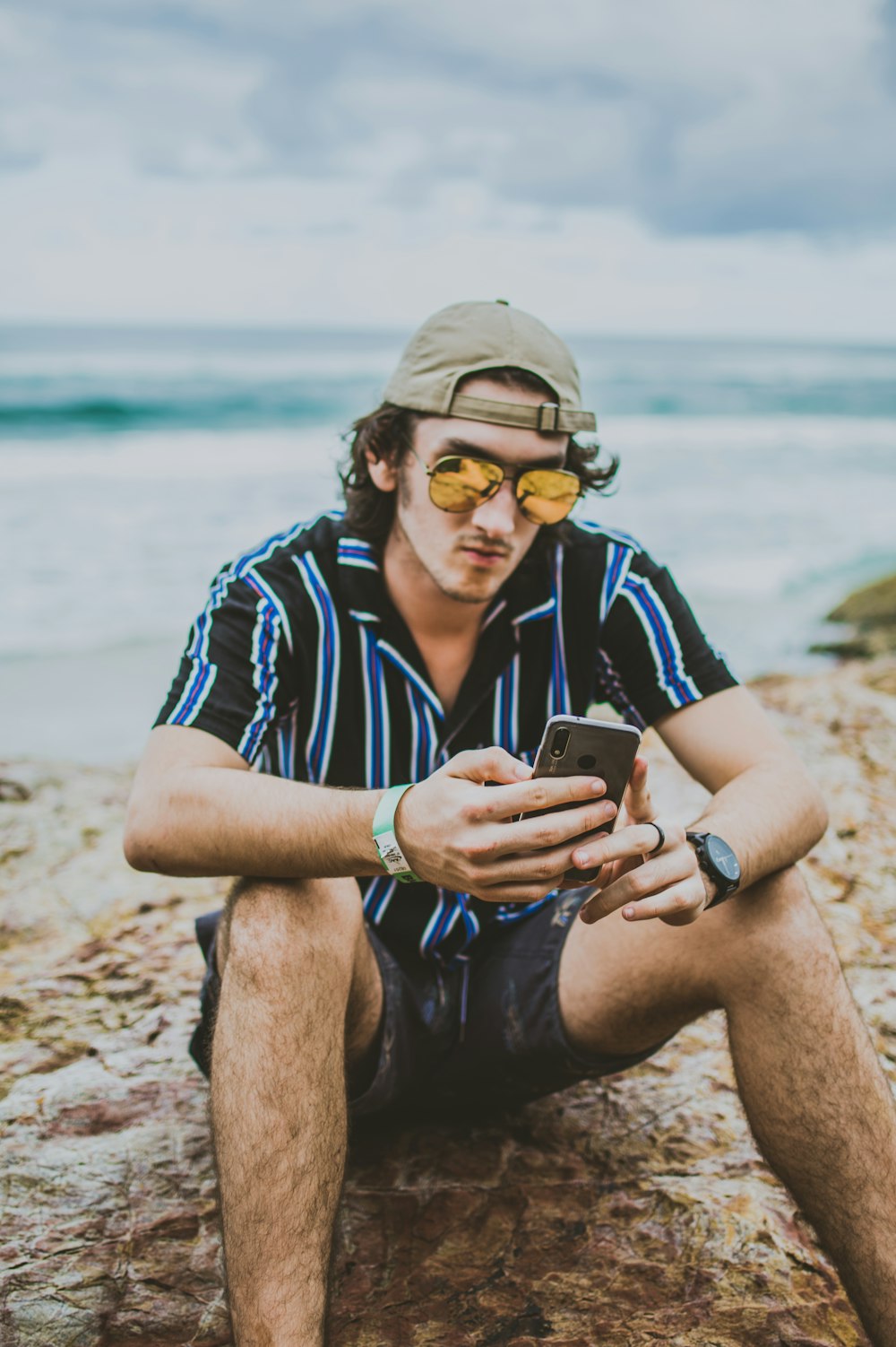Mann hält Smartphone in der Hand, während er auf Sand sitzt